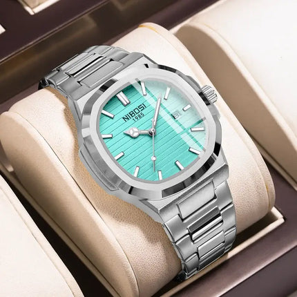 Luxury quartz watch with silver band and turquoise dial, styled on a display cushion.